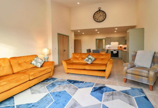 Woonkamer in Little Rissington - Barn Four met gele zetels, grote wandklok en modern blauw tapijt.
