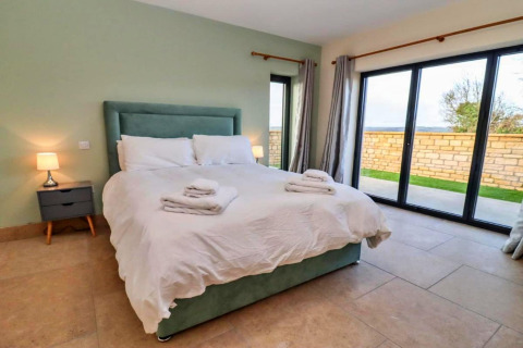 Moderne slaapkamer met dubbel bed, nachtkastjes en grote ramen in Little Rissington - Barn Four, VK.
