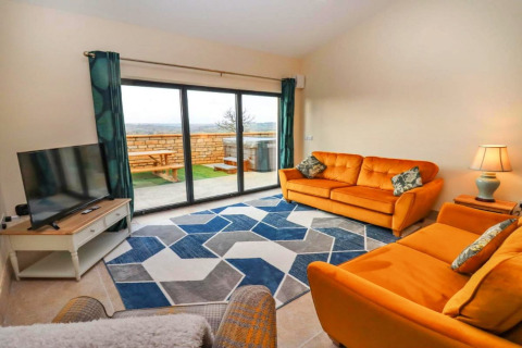 Heldere woonkamer in Little Rissington - Barn Four met oranje zetels, geometrisch tapijt en terraszicht.