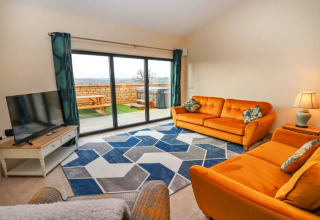Heldere woonkamer in Little Rissington - Barn Four met oranje zetels, geometrisch tapijt en terraszicht.