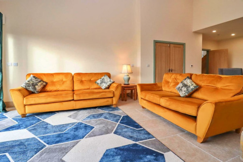 Knusse woonkamer bij Little Rissington - Barn Four, VK, met twee oranje zetels en een blauw vloerkleed.