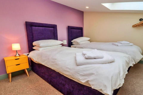 Slaapkamer bij Little Rissington - Barn Four met twee eenpersoonsbedden, paarse hoofdborden en gele nachttafel.