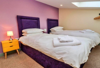 Slaapkamer bij Little Rissington - Barn Four met twee eenpersoonsbedden, paarse hoofdborden en gele nachttafel.