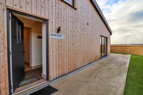 Ingang van Little Rissington - Barn Four lodge met open deur, houten gevelbekleding en tuinzicht.