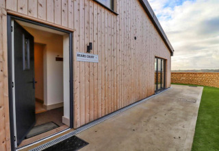 Ingang van Little Rissington - Barn Four lodge met open deur, houten gevelbekleding en tuinzicht.