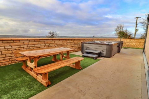 Buitenzone van Little Rissington - Barn Four in het VK met houten picknicktafel en jacuzzi.