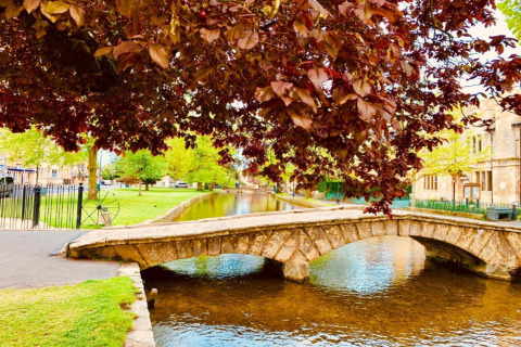Stenen brug over een vredige rivier met groene bomen in de buurt van Little Rissington, Verenigd Koninkrijk.