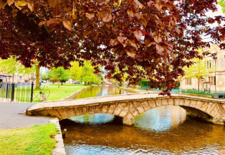 Stenen brug over een vredige rivier met groene bomen in de buurt van Little Rissington, Verenigd Koninkrijk.