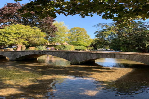Stenen brug over ondiep water bij Little Rissington - Barn Four Lodge, omgeven door groene bomen in Engeland.