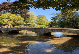 Stenen brug over ondiep water bij Little Rissington - Barn Four Lodge, omgeven door groene bomen in Engeland.