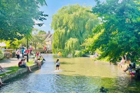 Mensen genieten aan de ondiepe rivier bij Little Rissington - Barn Four, omringd door groen en bomen.