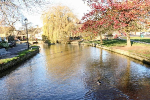 Vredige rivier bij Little Rissington - Barn Four Lodge, met eenden, herfstbomen en groene wandelpaden.