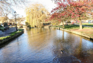 Vredige rivier bij Little Rissington - Barn Four Lodge, met eenden, herfstbomen en groene wandelpaden.