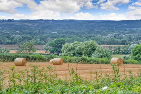 Uitzicht op velden met hooibalen, bomen en heuvels bij Little Rissington - Barn Four, Verenigd Koninkrijk.
