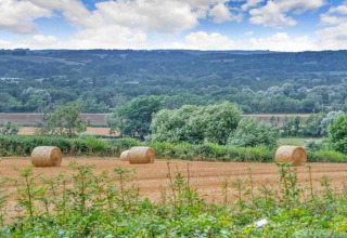 Uitzicht op velden met hooibalen, bomen en heuvels bij Little Rissington - Barn Four, Verenigd Koninkrijk.