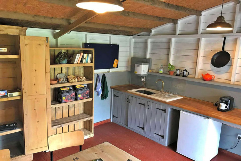Pequeña cocina acogedora en una tienda tipi con estanterías de madera, fregadero y nevera.