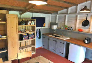 Cozy kitchenette in a teepee tent with wooden shelves, a fridge, sink, pan, and warm lighting.