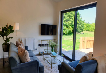 Moderne woonkamer in Blackbarn Wood lodge, UK, met blauwe banken en zicht op groene tuin via schuifpui