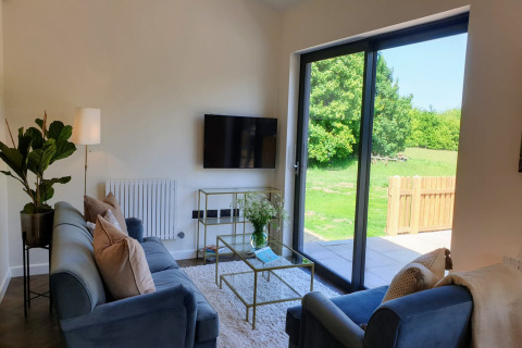 Soggiorno moderno presso Blackbarn Wood, Regno Unito, con divani blu, vetrate e vista sul verde
