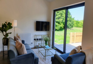 Soggiorno moderno presso Blackbarn Wood, Regno Unito, con divani blu, vetrate e vista sul verde
