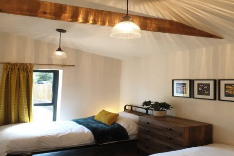 Camera da letto al lodge Blackbarn Wood, Regno Unito, con due letti singoli, tenda gialla e cassettiera in legno.