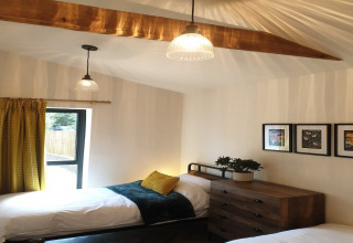 Camera da letto al lodge Blackbarn Wood, Regno Unito, con due letti singoli, tenda gialla e cassettiera in legno.