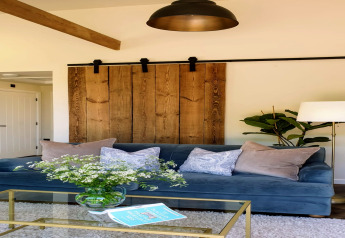 Woonkamer met blauwe bank, kussens, houten schuifdeur, vloerlamp en glazen tafel in Blackbarn Wood, VK.