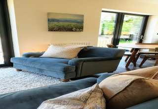 Soggiorno al lodge Blackbarn Wood nel Regno Unito, divano blu, tappeto chiaro e vista sul giardino.