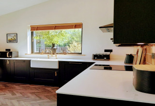 Cucina moderna con mobili neri, piani bianchi e finestra nella lodge Blackbarn Wood nel Regno Unito.