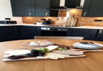 Moderne keuken in Blackbarn Wood Lodge, VK, met kaas, brood en fruit op een plank op tafel.