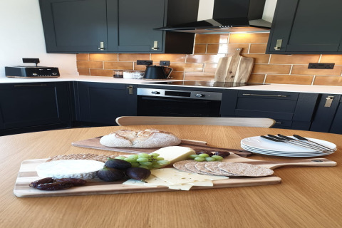 Cucina moderna al Blackbarn Wood Lodge, Regno Unito, con vassoio di formaggi, pane e frutta sul tavolo.