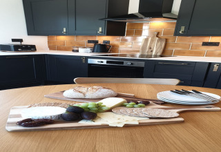 Cucina moderna al Blackbarn Wood Lodge, Regno Unito, con vassoio di formaggi, pane e frutta sul tavolo.