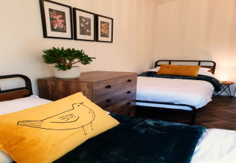 Twee eenpersoonsbedden met gele vogel-kussens bij Blackbarn Wood lodge, VK. Houten ladekast en muurkunst.