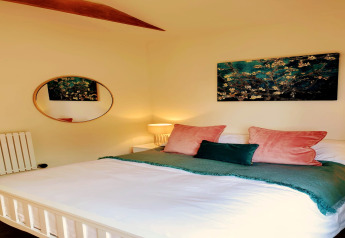 Slaapkamer met tweepersoonsbed, groene en roze kussens, wandkunst en ronde spiegel in Blackbarn Wood lodge, VK.