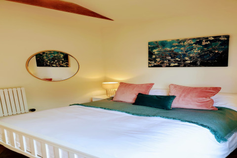 Camera da letto con letto matrimoniale, cuscini verdi e rosa, arte murale e specchio rotondo a Blackbarn Wood lodge.