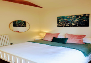 Camera da letto con letto matrimoniale, cuscini verdi e rosa, arte murale e specchio rotondo a Blackbarn Wood lodge.