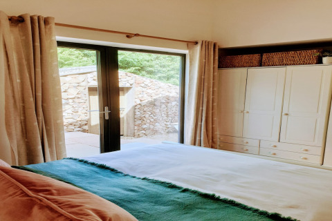 Camera da letto accogliente con porte in vetro, armadio e vista sul muro di pietra al Blackbarn Wood Lodge UK.