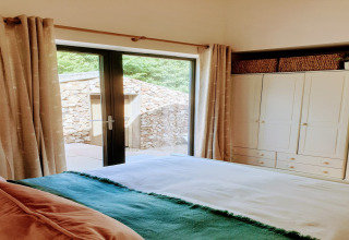 Camera da letto accogliente con porte in vetro, armadio e vista sul muro di pietra al Blackbarn Wood Lodge UK.