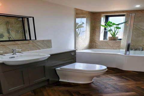 Bagno moderno al lodge Blackbarn Wood nel Regno Unito, con vasca, pianta e pavimento a spina di pesce.