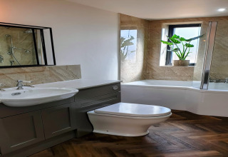 Bagno moderno al lodge Blackbarn Wood nel Regno Unito, con vasca, pianta e pavimento a spina di pesce.