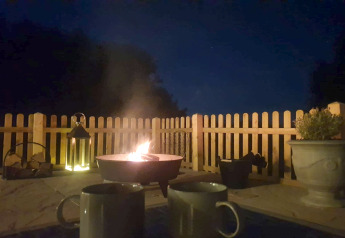 Avondsfeer bij Blackbarn Wood lodge met vuurkorf, twee mokken, lantaarn en houten schutting.