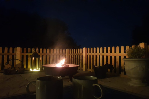 Fuoco serale alla lodge Blackbarn Wood, con due tazze, lanterna e recinto di legno nel Regno Unito.