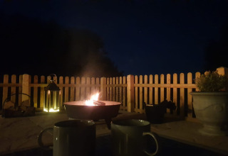 Fuoco serale alla lodge Blackbarn Wood, con due tazze, lanterna e recinto di legno nel Regno Unito.
