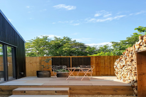 Terrazza esterna al Blackbarn Wood lodge nel Regno Unito, con sedie, legna e recinzione in legno.