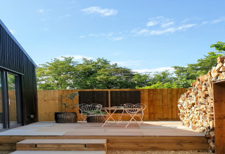 Terrazza esterna al Blackbarn Wood lodge nel Regno Unito, con sedie, legna e recinzione in legno.