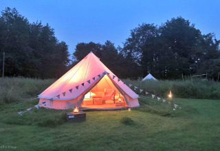A cozy teepee tent glows with warm light at dusk on a grassy field, decorated with bunting and lanterns.