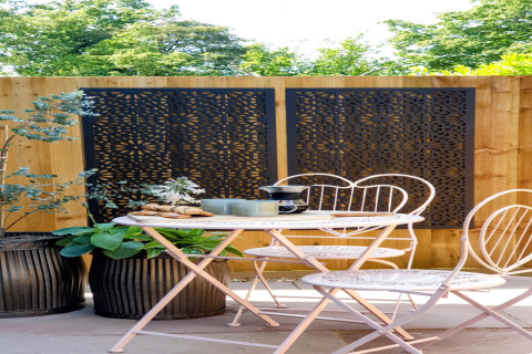 Area salotto esterna presso Blackbarn Wood nel Regno Unito con sedie bianche e pannelli decorativi neri.