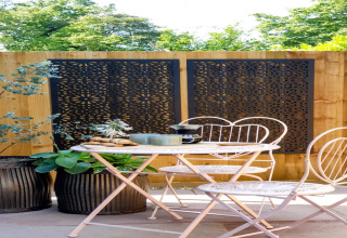 Area salotto esterna presso Blackbarn Wood nel Regno Unito con sedie bianche e pannelli decorativi neri.
