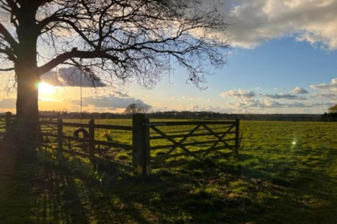 Sunset over a green field with a tree, wooden fence, and tire swing, viewed from a teepee tent site.