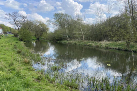 View from a teepee tent of a tranquil river with lush grass, trees, and sky reflecting on the water.